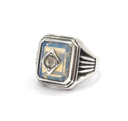 Close front view tilted right, the milky bluish opaline rectangle filling its stepped bezel with the round colourless paste held in a lozenge-shaped prong setting at its centre, ribbed shoulder alongside.