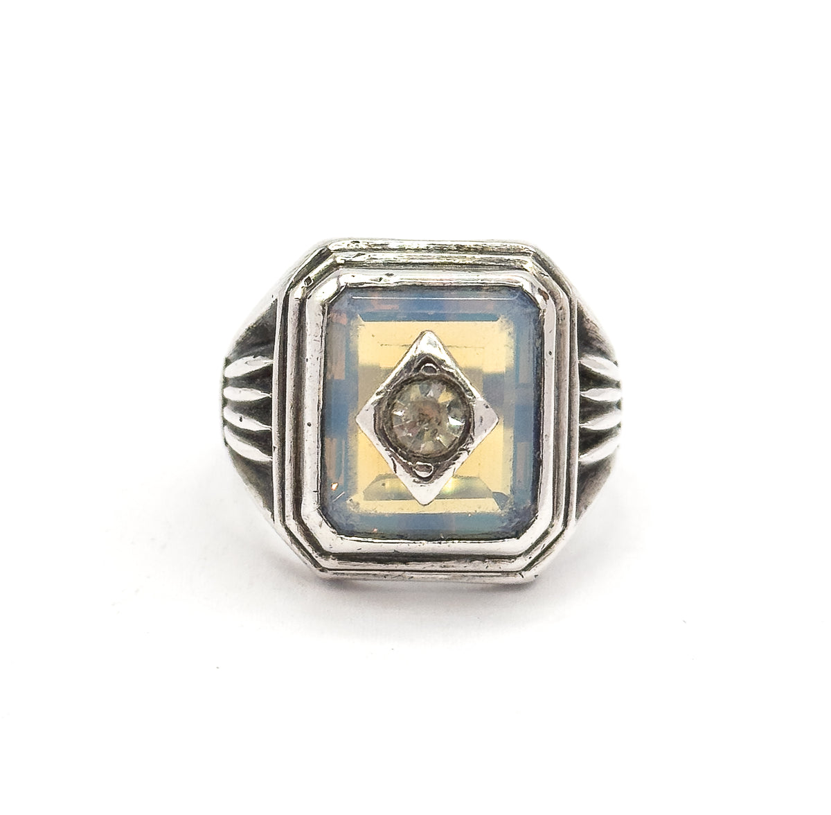 Straight-on overhead view of the signet-style face, the stepped rectangular bezel squared to the camera with the opaline glass and central prong-set paste symmetrical between the fanned ribbed shoulders.