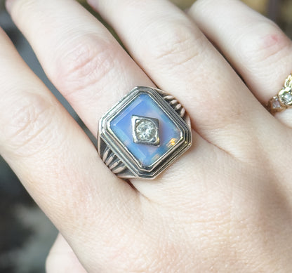 Close view from above of the ring shown on a finger, the bezel-set opaline glass filling the face with the prong-set paste at its centre.