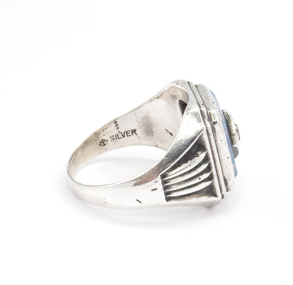 Side view of the ring resting on a white surface, showing the ribbed shoulder rising to the bezel and the stamped mark inside the shank reading SILVER beside a small maker's mark.