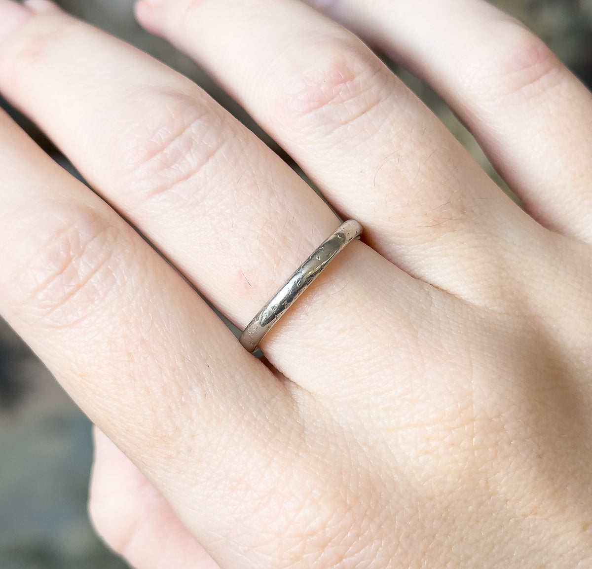 Shown on a finger from above, the narrow band sits low between the knuckles, its engraved surface reading as faint light markings across the domed shank.