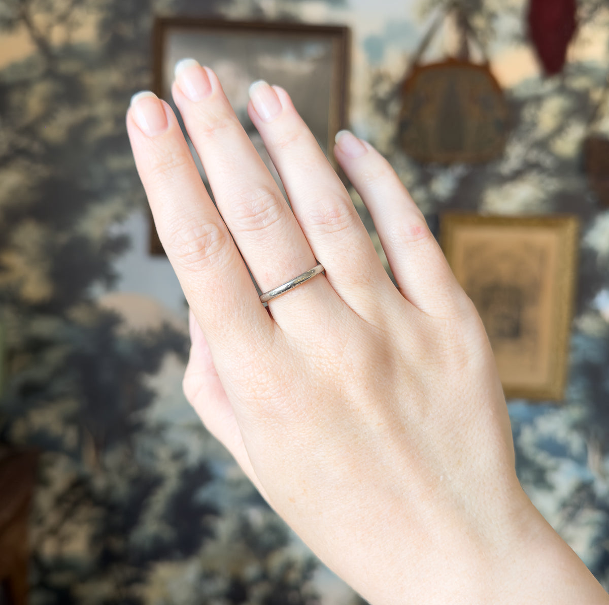 The hand is raised with fingers together against a soft blue-grey backdrop, the slim band circling the ring finger and giving a clear sense of its narrow width.