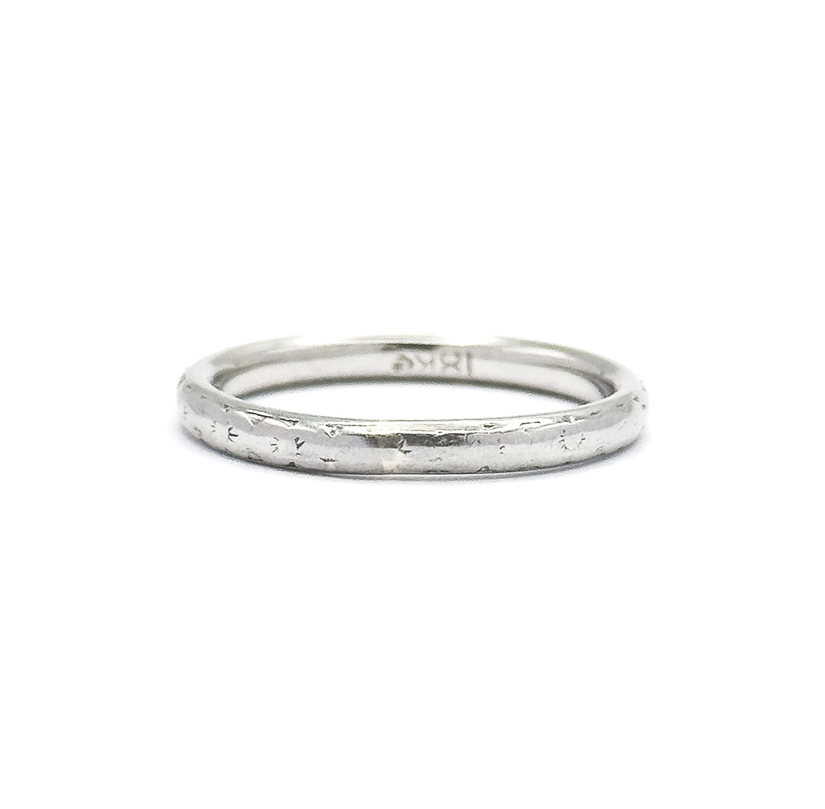 The ring stands upright on a white background, showing the full circle of the narrow domed shank with faint engraved marks along the outside and a stamp inside.