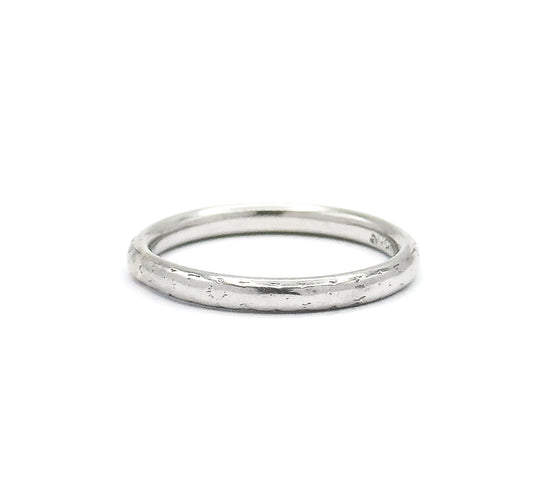 Seen almost edge-on against white, the band reads as a slim flattened oval, its domed outer surface catching light along the front of the shank with faint engraved texture.