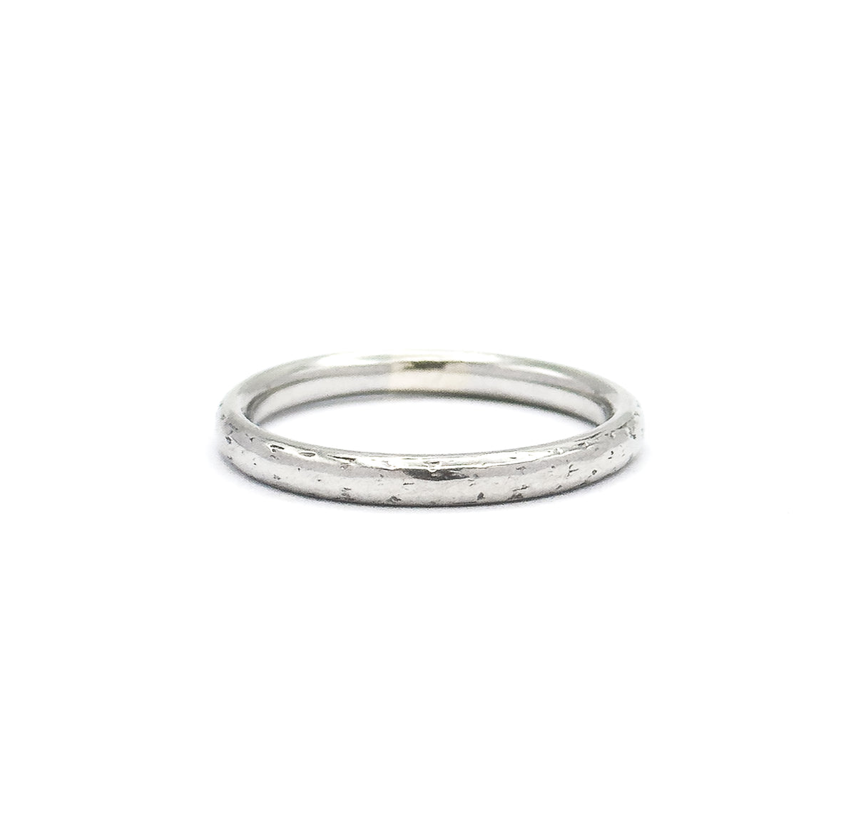 The band sits low against white, its opening reduced to a thin ellipse along the top while the full front face of the domed shank fills the view, speckled with faint engraved texture.