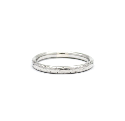 The band sits low against white, its opening reduced to a thin ellipse along the top while the full front face of the domed shank fills the view, speckled with faint engraved texture.