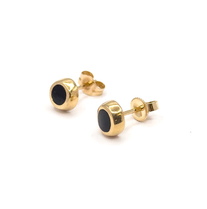 Both studs angle away to the right at eye level, showing the deep drum-like side wall of each yellow gold bezel, with one butterfly back turned flat and the other edge-on.