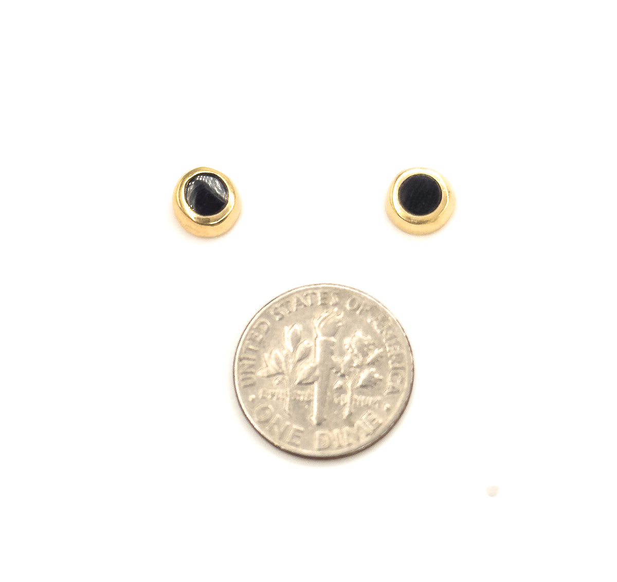 The pair sits face-up on white above a dime, each round black enamel disc ringed by a polished yellow gold bezel, the coin showing they are a little smaller across.