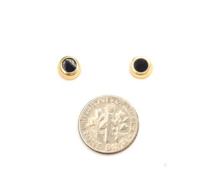 The pair sits face-up on white above a dime, each round black enamel disc ringed by a polished yellow gold bezel, the coin showing they are a little smaller across.