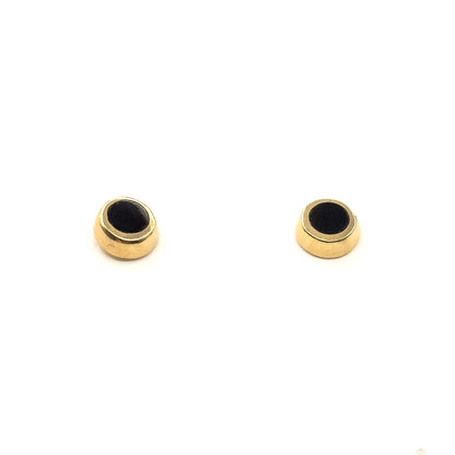 The pair stands upright on white, tilted so the rounded yellow gold side walls and the depth of each bezel are visible beneath the black enamel faces.
