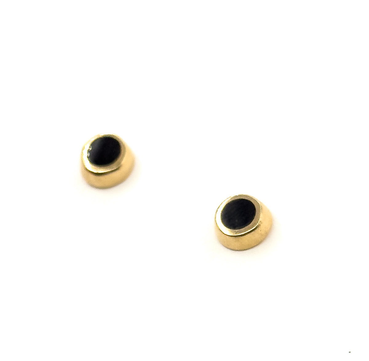 The two studs float on plain white at an angle, catching light across the polished yellow gold bezel rims so each black enamel face reads as a shallow disc.