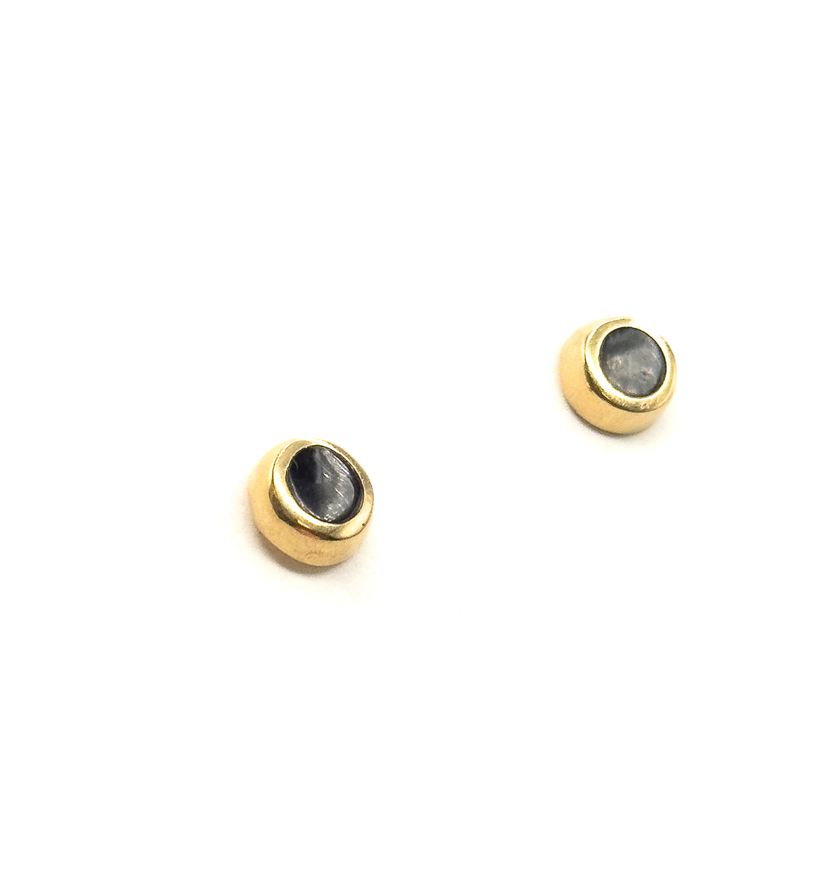 The two studs sit apart on white, each turned three-quarter so the yellow gold bezel appears thicker along one side of the black enamel face.