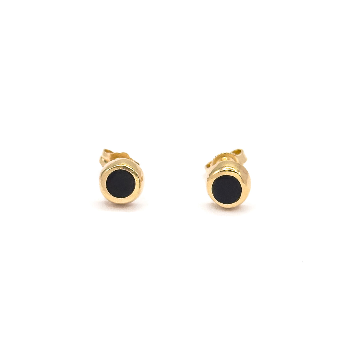 The pair stands side by side facing forward, the yellow gold post and butterfly back of each stud rising visibly behind the bezelled black enamel face.