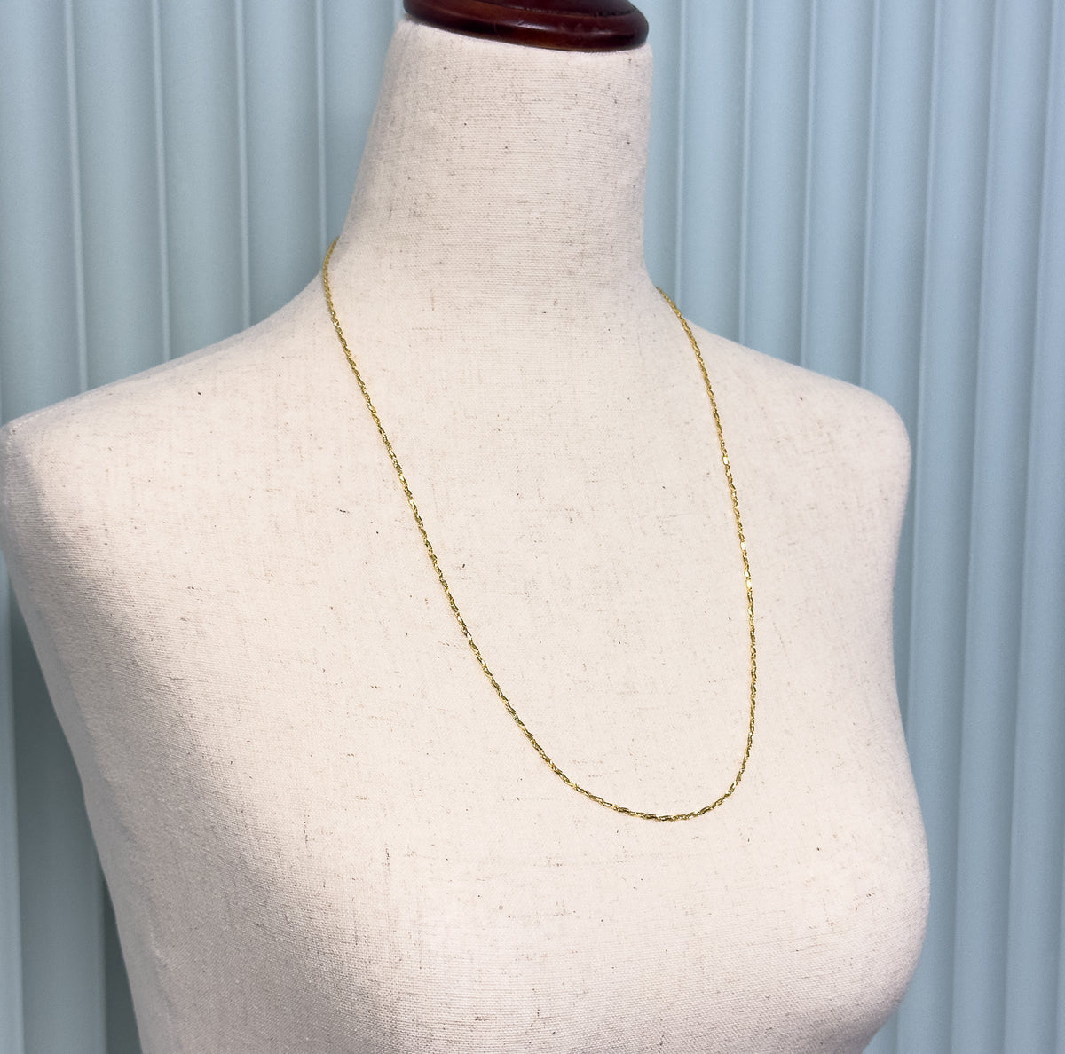 Angled view showing the slender chain looping in a long U across the bust's chest, the flat crinkle links catching light along their length.