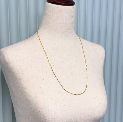 Angled view showing the slender chain looping in a long U across the bust's chest, the flat crinkle links catching light along their length.