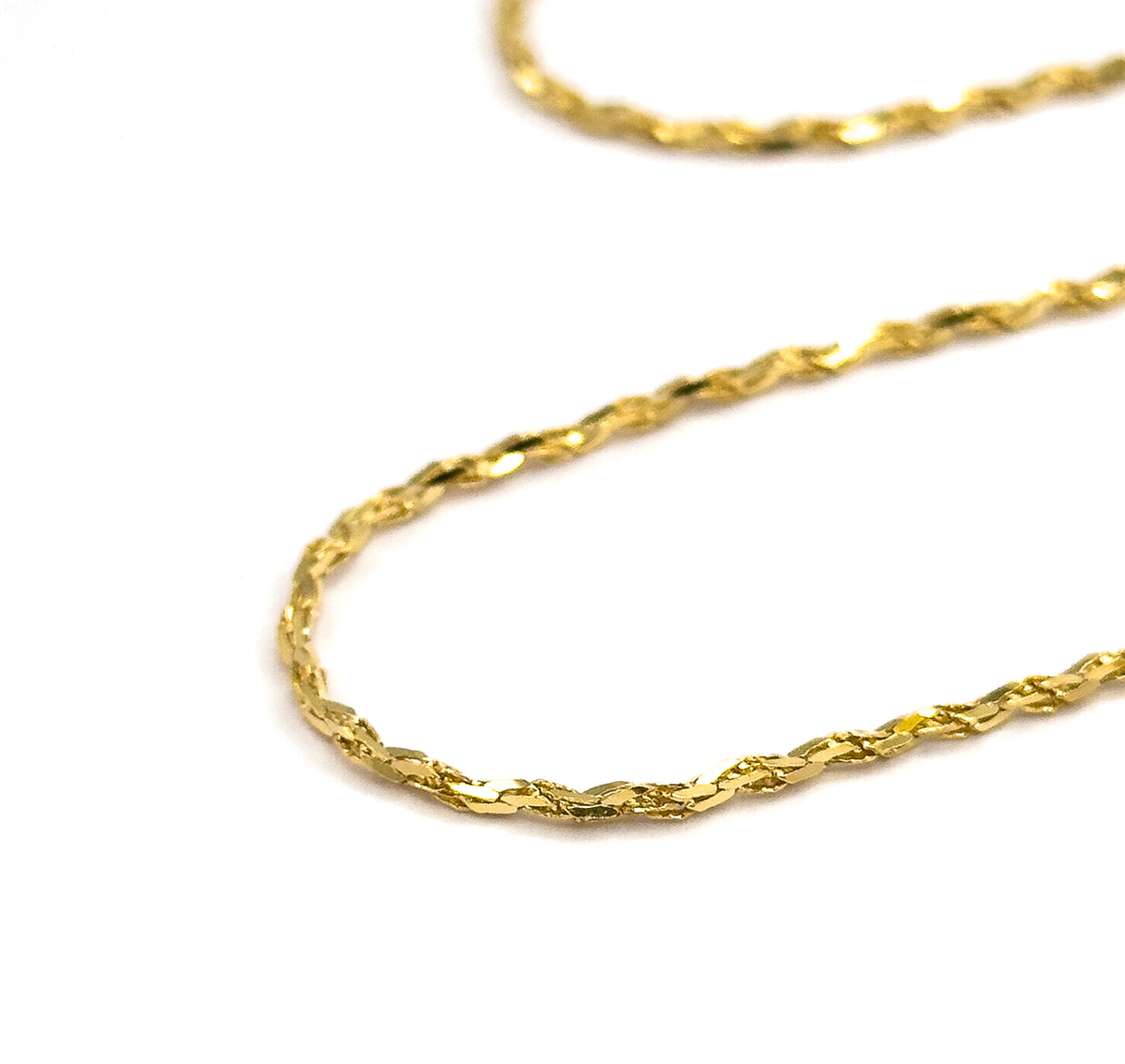 Two sweeping curves of the crinkle chain draped in a wide U across white, the lower run in sharp focus and the upper one softly blurred behind it, showing how the chain falls.
