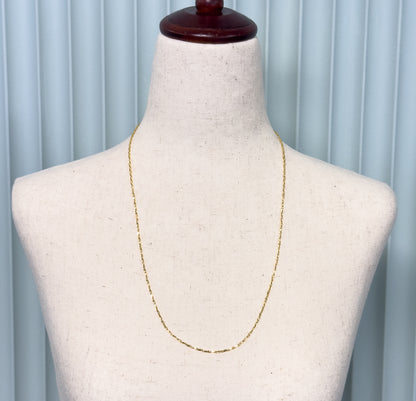 A 14K yellow gold crinkle link chain necklace shown draped at the neck of a pale linen display bust against a soft blue background.