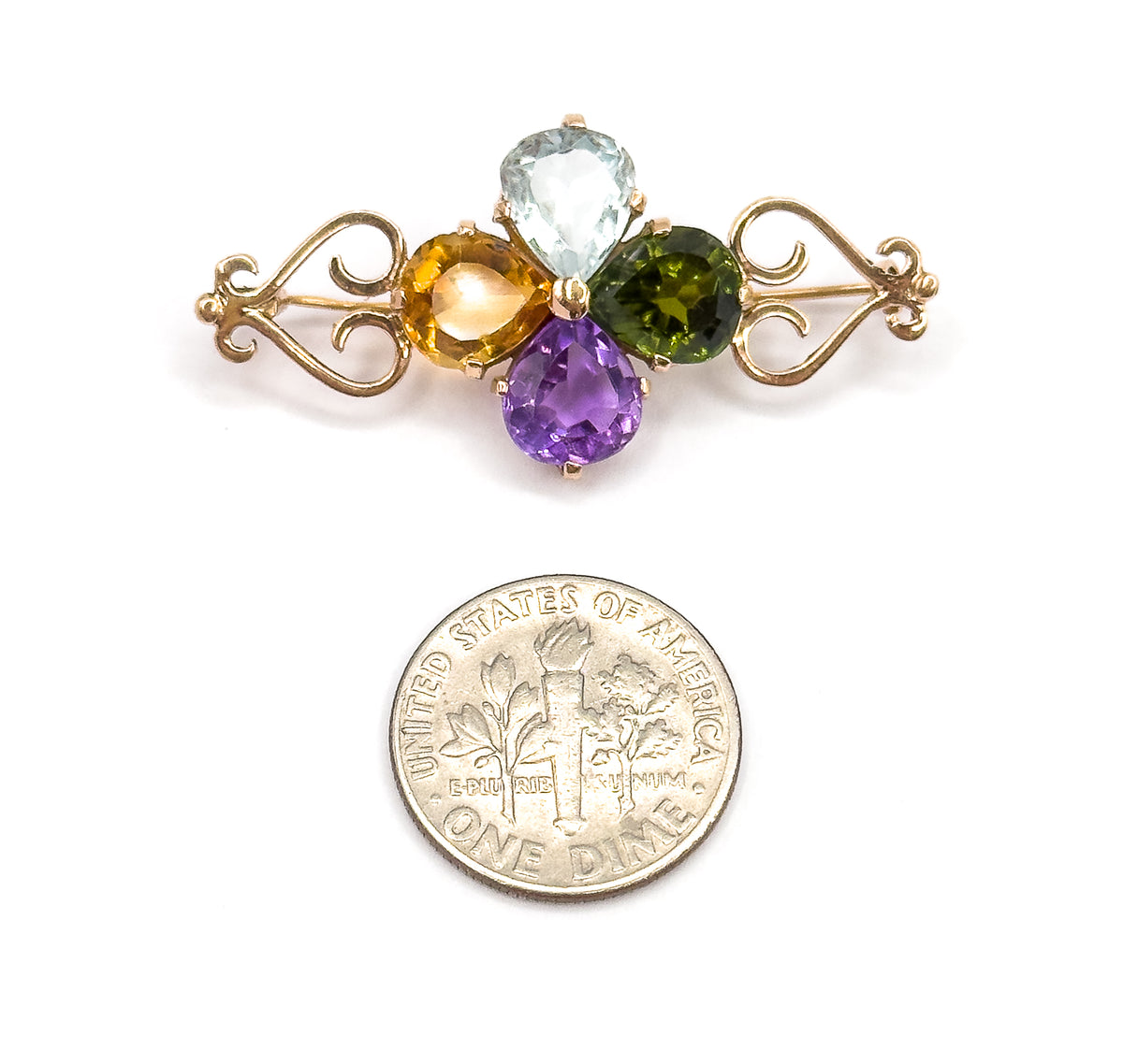 Face-up view with a dime placed below for scale, the brooch about twice the coin's width, its four pear stones and rose gold scrolls facing the camera.