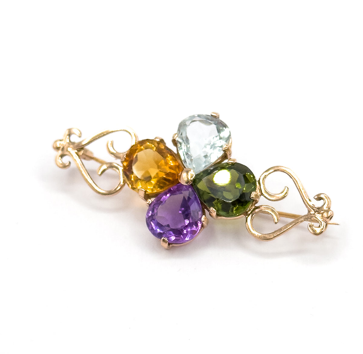 Higher angled view looking down onto the clover, the pale blue, green, yellow and purple pear stones grouped in their prongs while the pin stem runs out behind the right rose gold scroll.