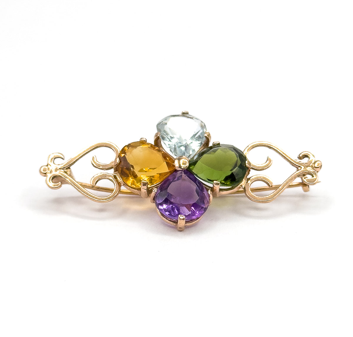 Low eye-level view from the front, the four pear stones standing proud of their prongs in a clover while the rose gold scroll arms sweep out level to each side against white.