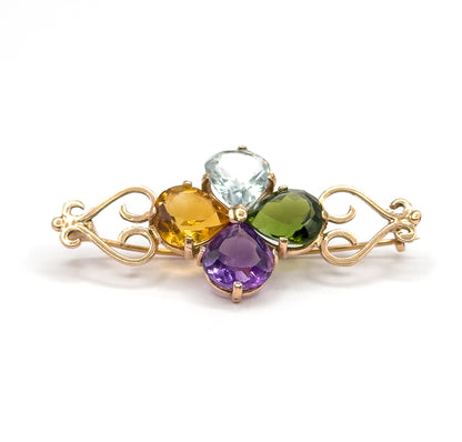 Low eye-level view from the front, the four pear stones standing proud of their prongs in a clover while the rose gold scroll arms sweep out level to each side against white.