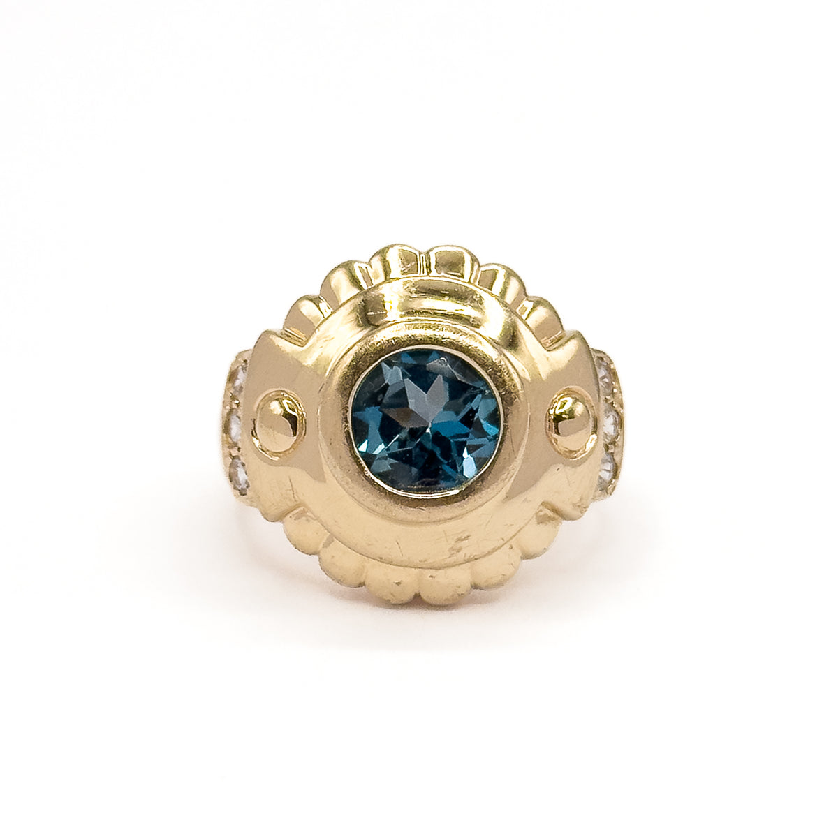 Straight down onto the face, the round London blue topaz centred in its bezel with a scalloped crest above and below and a gold bead plus prong-set white sapphires on each shoulder.