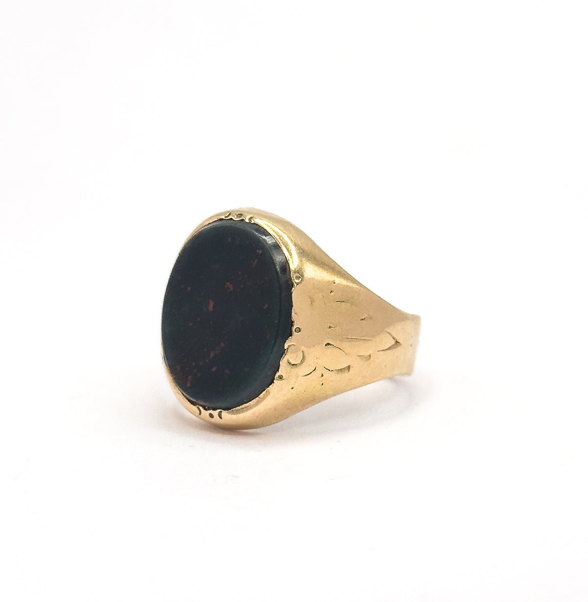 Angled three-quarter view with the oval bloodstone face tilted toward the viewer, its dark green surface flecked with red, while the engraved right shoulder widens into the yellow gold shank.