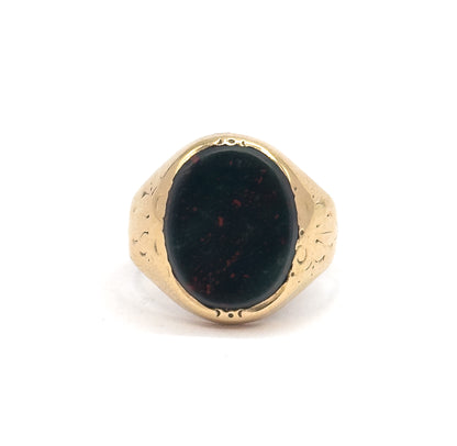 Close frontal view cropped tight on the bezel, the oval bloodstone's red speckles scattered over dark green, with small punched marks visible at the top and bottom of the gold rim.