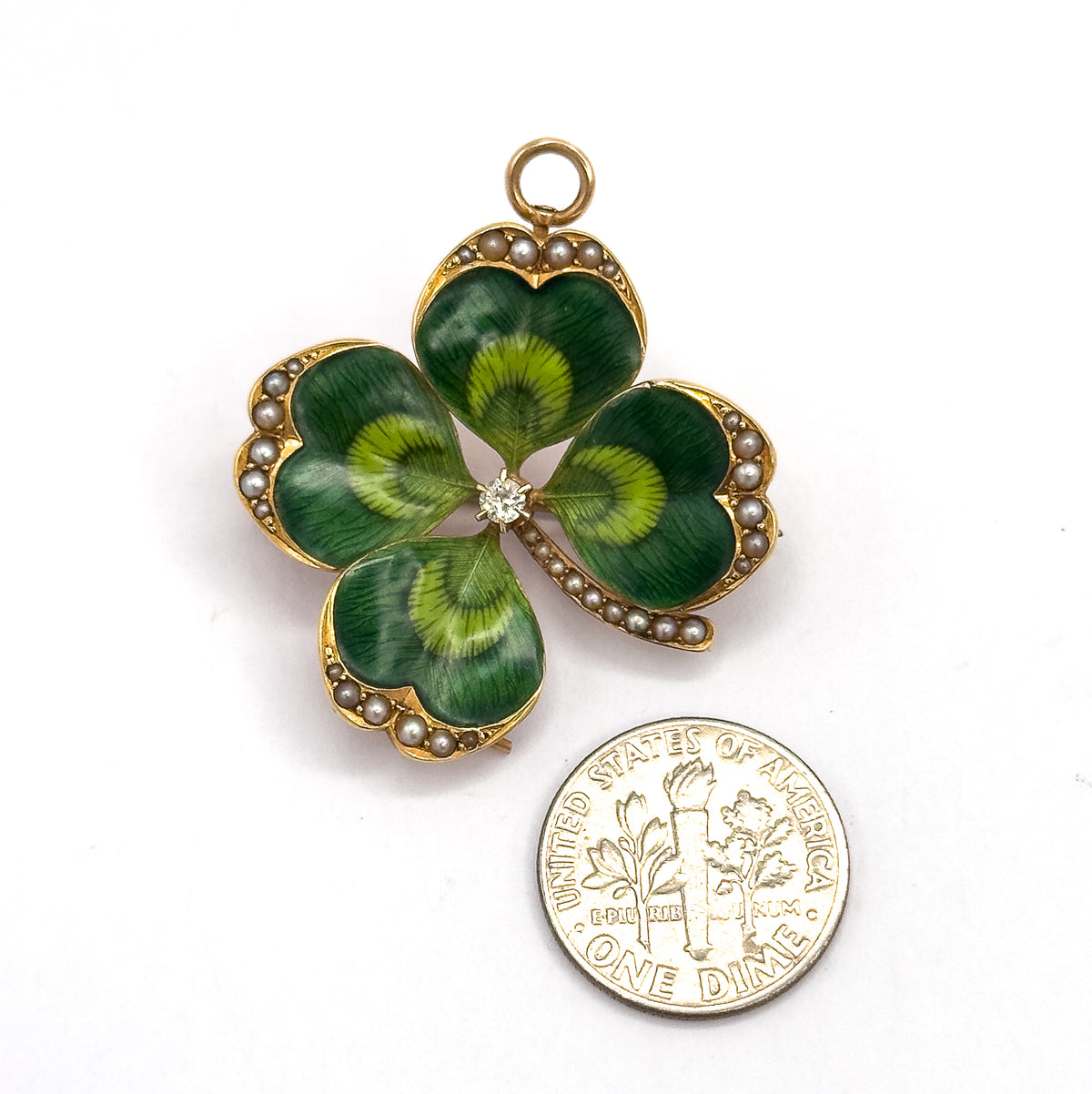 Flat front view on white beside a dime for scale, the clover barely larger than the coin, its four green enamelled leaves edged in seed pearls around the prong-set centre diamond.