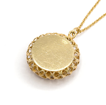 The smooth flat back of the pendant angled up on a white ground, its lattice gallery rimming the edge, a small crown stamp near the bail where the chain attaches.