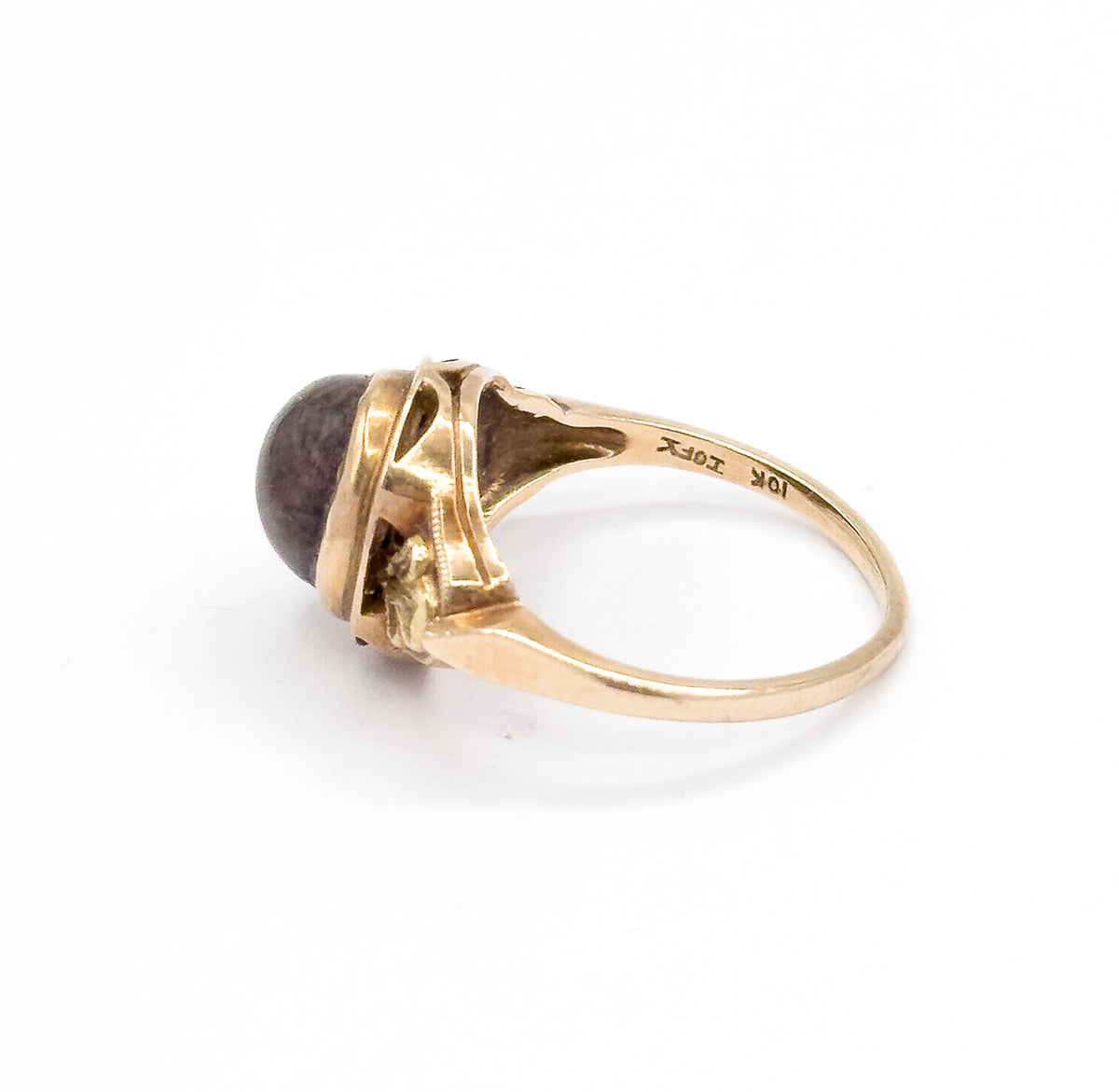 Lying tilted on white with the shank facing the camera, this angle shows the small stamps struck inside the band and the openwork gallery holding the brown cabochon at the far end.