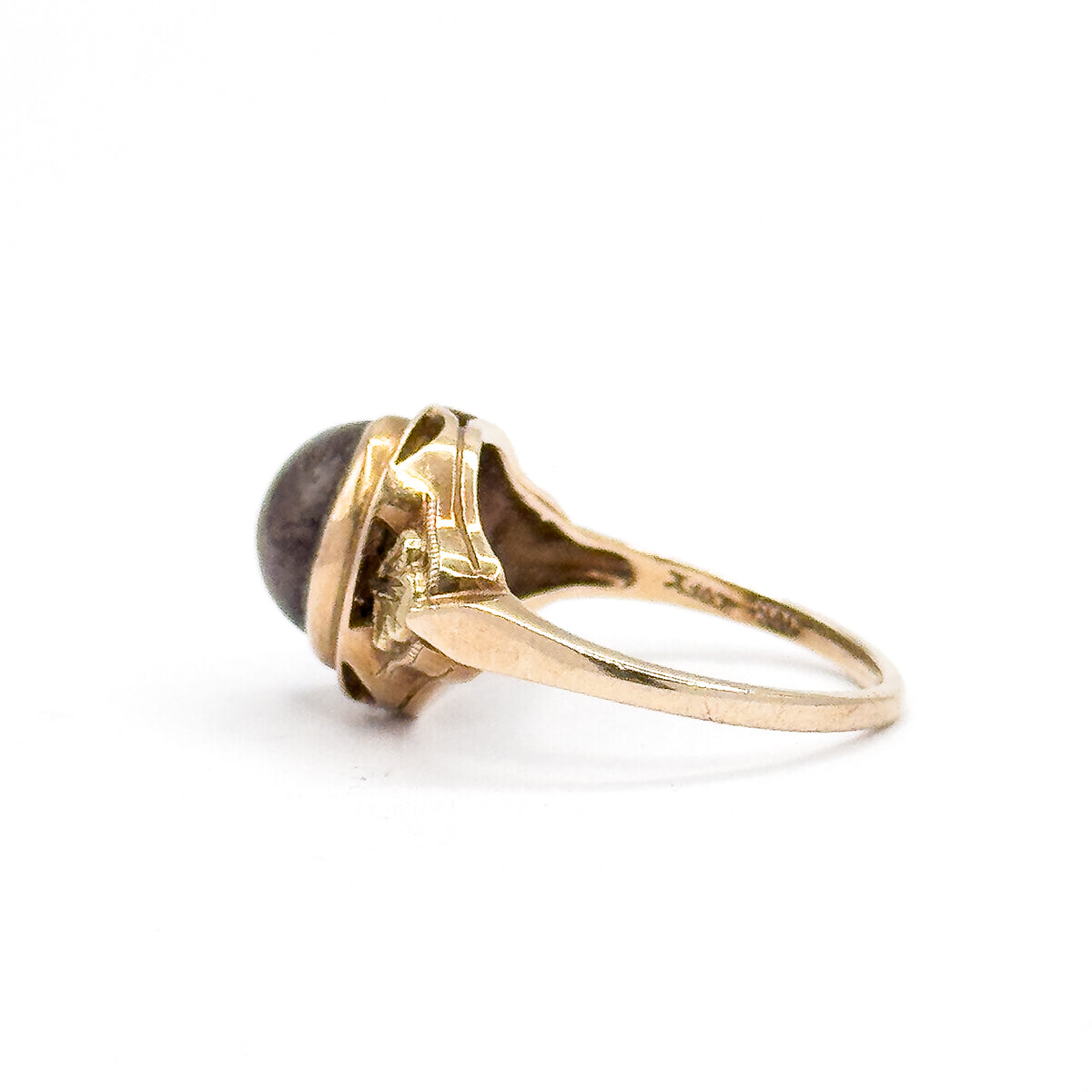 Opposite side profile against white, the bezel rim circling the brown cabochon while the openwork gallery and shoulder details lead into the shank, where faint stamps catch the light.