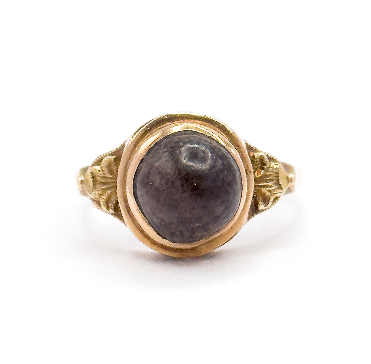 Straight-on top view against white, the round brown cabochon filling its smooth rose gold bezel, with leaf-like decorative details spreading across the shoulders on each side.