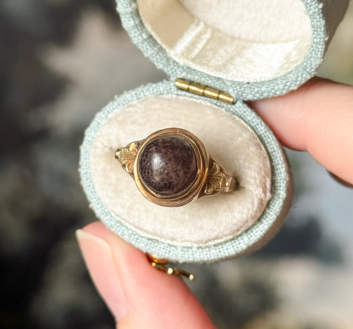 Closer view into the open box, the hinge visible at the top, showing the speckled surface of the brown cabochon and the leafy decoration running down each shoulder to the slim shank.