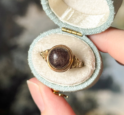 Closer view into the open box, the hinge visible at the top, showing the speckled surface of the brown cabochon and the leafy decoration running down each shoulder to the slim shank.