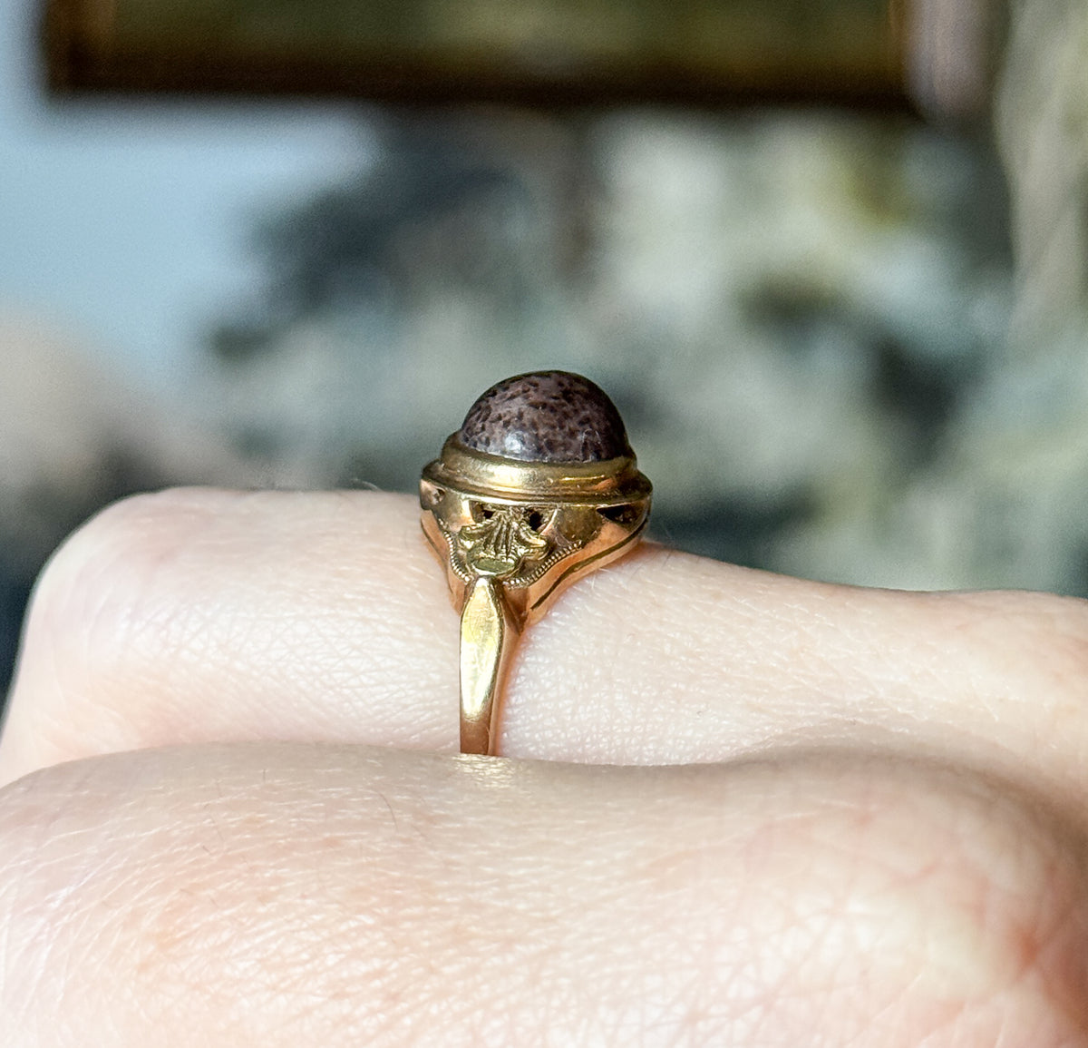 Shown on a finger from the side, so the bezel and openwork gallery stand clear of the skin, the speckled brown cabochon domed above the tapering shank.