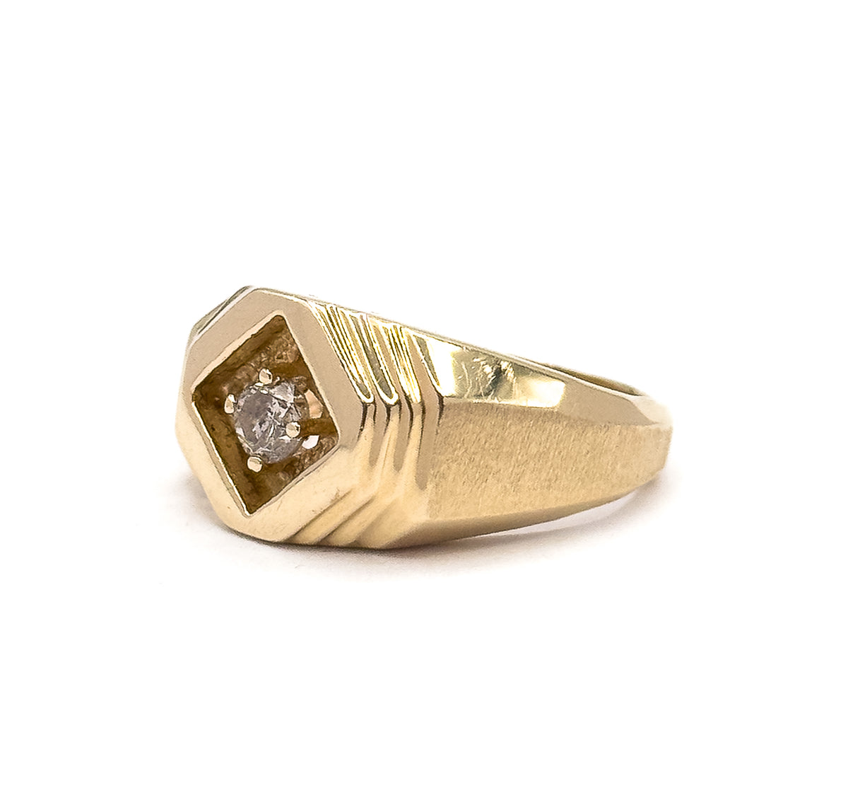A raised three-quarter view from the front corner, the recessed diamond-shaped face angled toward the viewer with its prong-set stone, stepped grooves and matte shoulder catching the light.