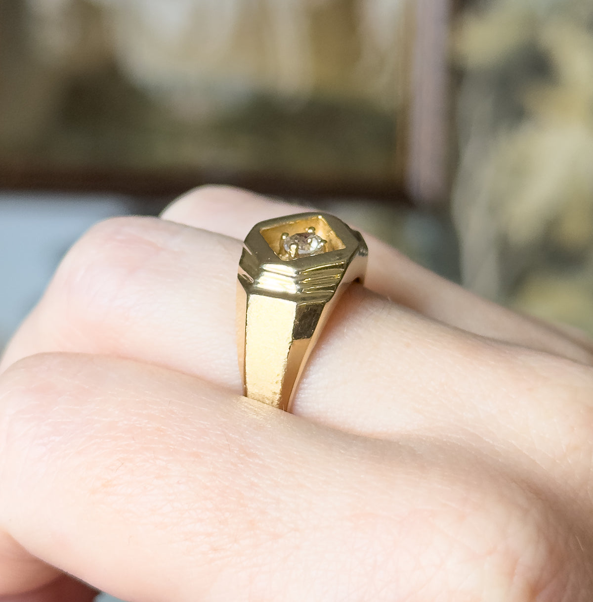 Angled close view on the finger, the low face and prong-set diamond catching the light while the flat stepped shoulders and tapering shank are seen from the side.