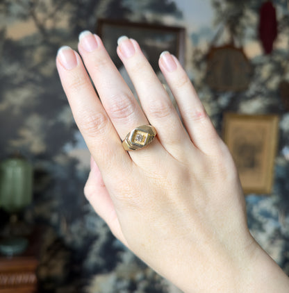 The whole hand is shown against a patterned backdrop, the ring small on the ring finger, giving a clear sense of its modest scale and low profile.