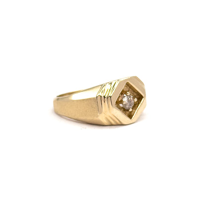 Off the hand now against a plain white background, the ring seen side-on in three-quarter view so the low face, prong-set diamond and grooved shoulders rise gently from the tapering shank.