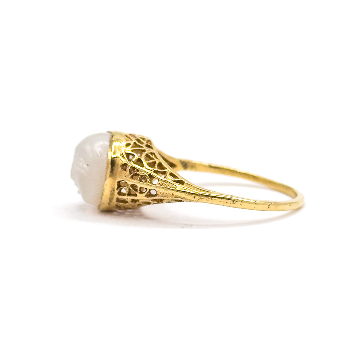 Low side view with the ring lying almost flat, the carved moonstone at left and the shank sweeping right, so the lacy filigree shoulder is seen edge-on in full length.