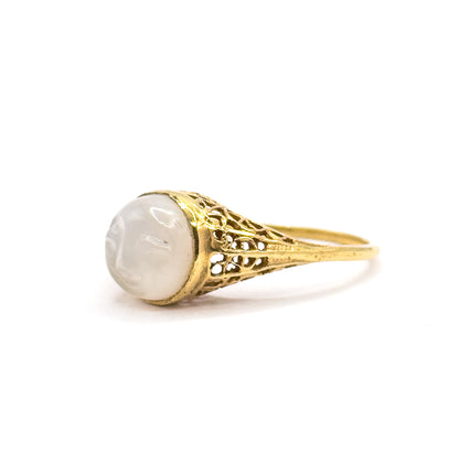 Side view from the left with the moonstone cabochon facing the camera, showing the bezel rim and the filigree shoulder flaring up from the slim shank behind it.