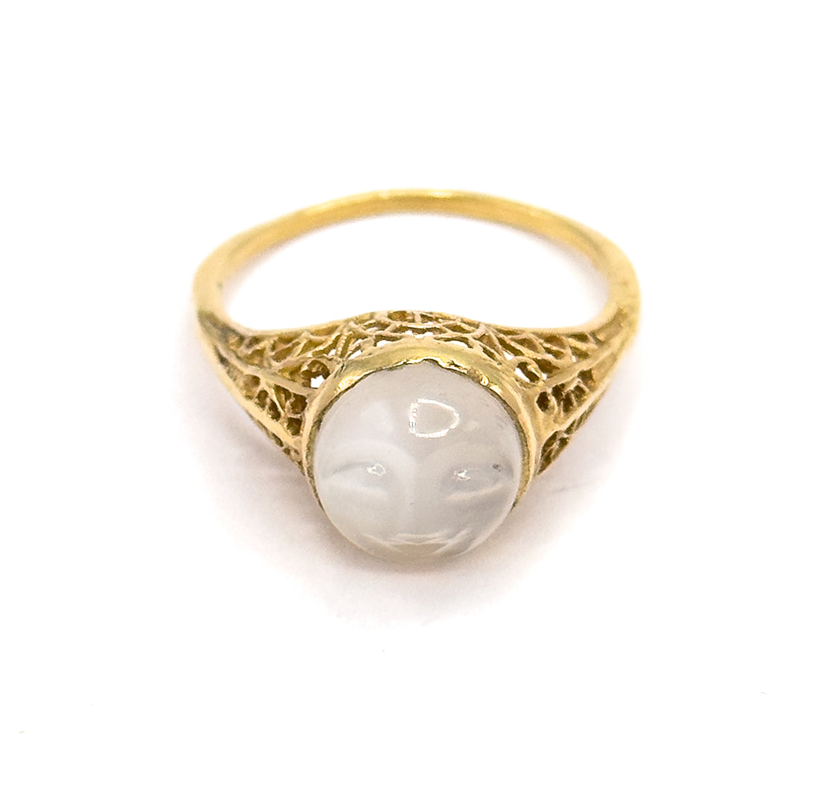 Top-down view against white with the carved moonstone face upright in its bezel, the filigree shoulders spreading symmetrically either side and the slim shank arching behind.