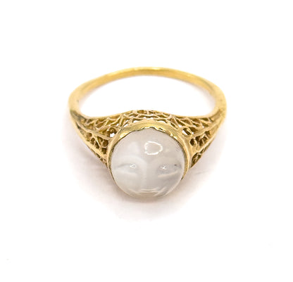 Top-down view against white with the carved moonstone face upright in its bezel, the filigree shoulders spreading symmetrically either side and the slim shank arching behind.