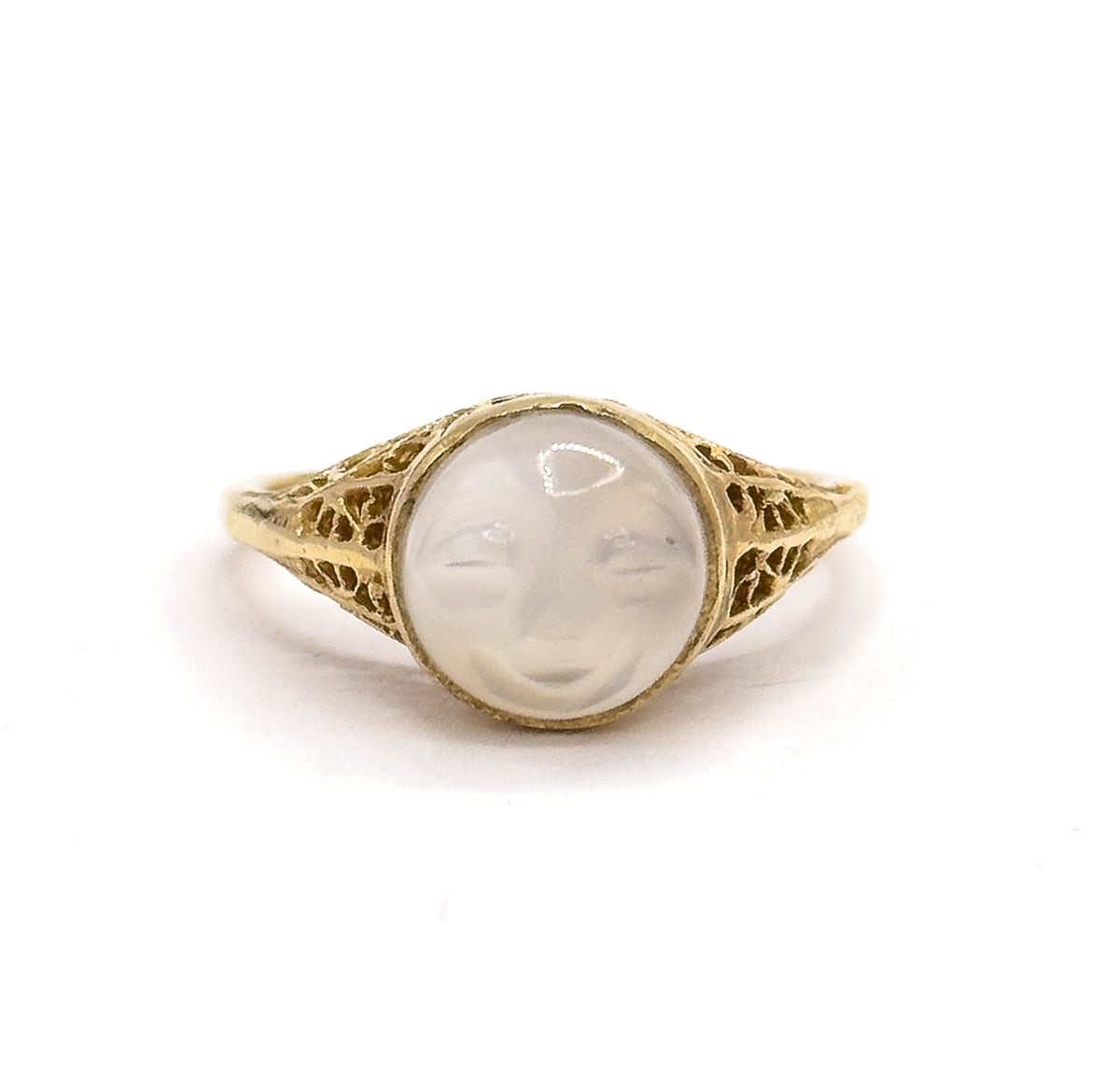 Close front view with the ring standing upright, filling the frame so the carved moonstone's closed eyes, nose and smiling mouth read clearly inside the bezel between the filigree shoulders.