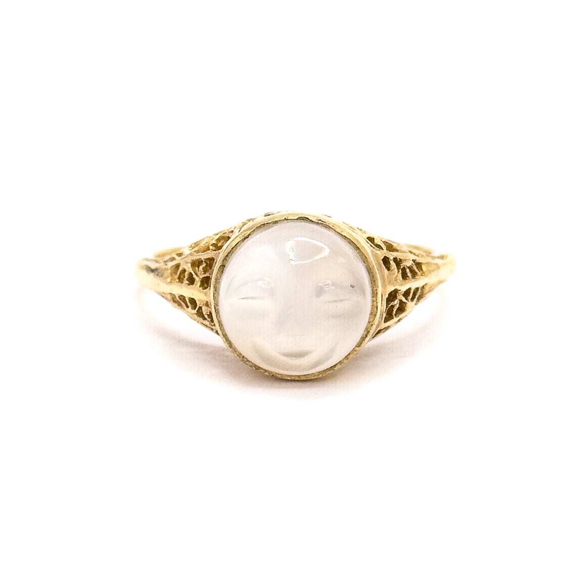 Upright front view from slightly further back, the whole ring small and centred on white so the carved moonstone face, its bezel and both filigree shoulders sit in balanced proportion.