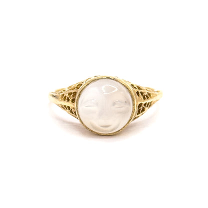 Upright front view from slightly further back, the whole ring small and centred on white so the carved moonstone face, its bezel and both filigree shoulders sit in balanced proportion.