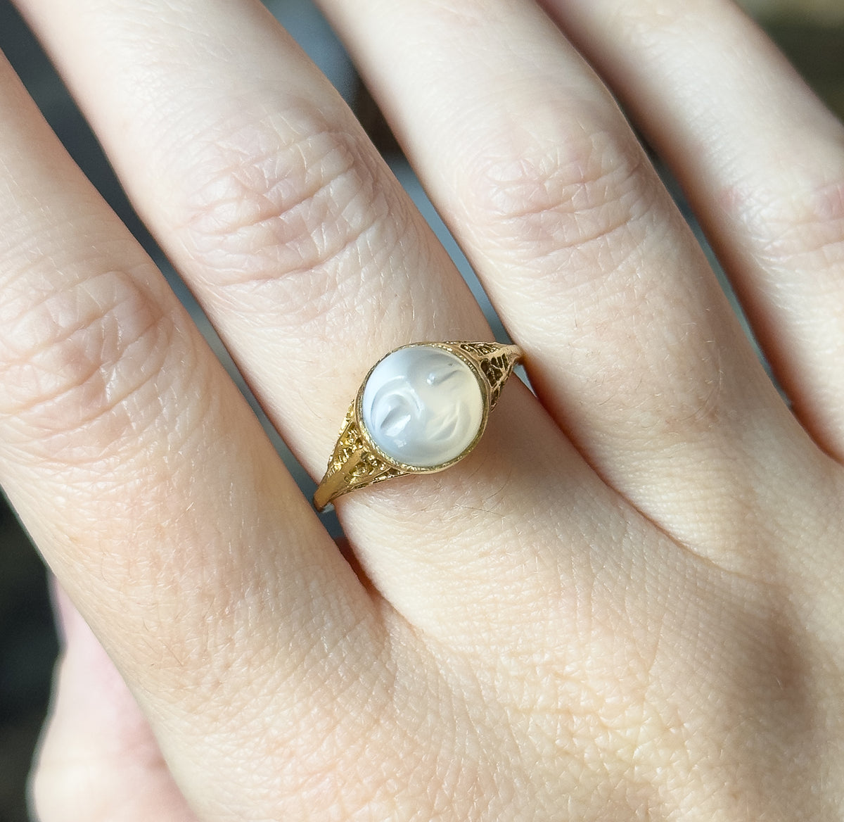 Shown on the hand with the fingers together, the moonstone cabochon and its gold bezel sitting low and compact across the finger, giving a clear sense of the ring's small scale.