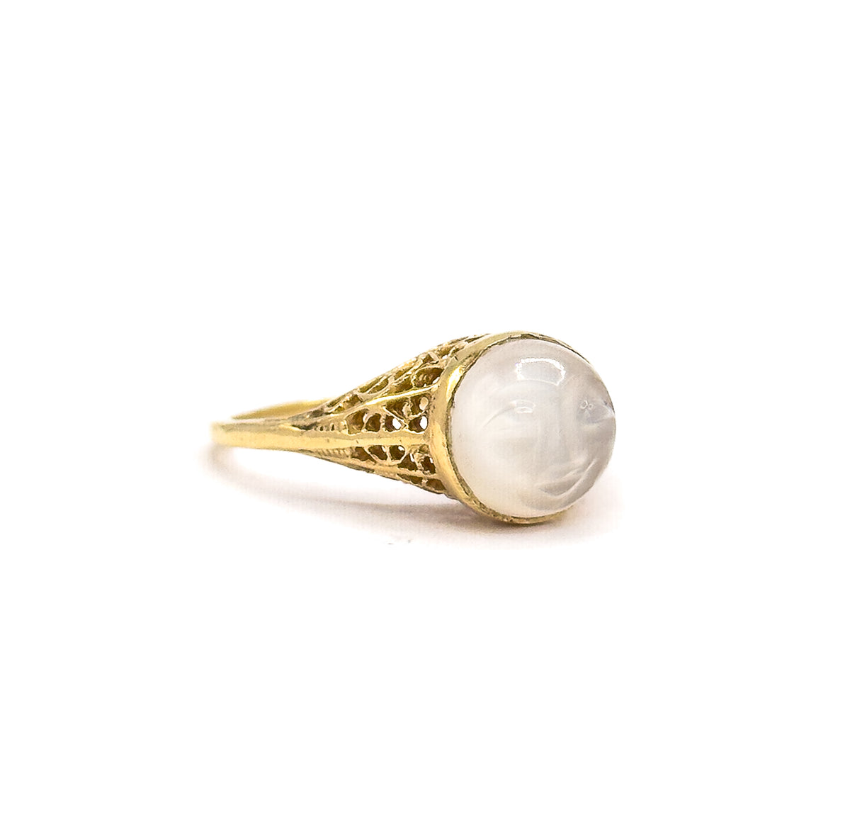Side profile against a plain white background, off the hand, showing the domed moonstone cabochon rising from its gold bezel above the pierced filigree gallery that tapers into a slim shank.