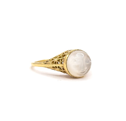Side profile against a plain white background, off the hand, showing the domed moonstone cabochon rising from its gold bezel above the pierced filigree gallery that tapers into a slim shank.